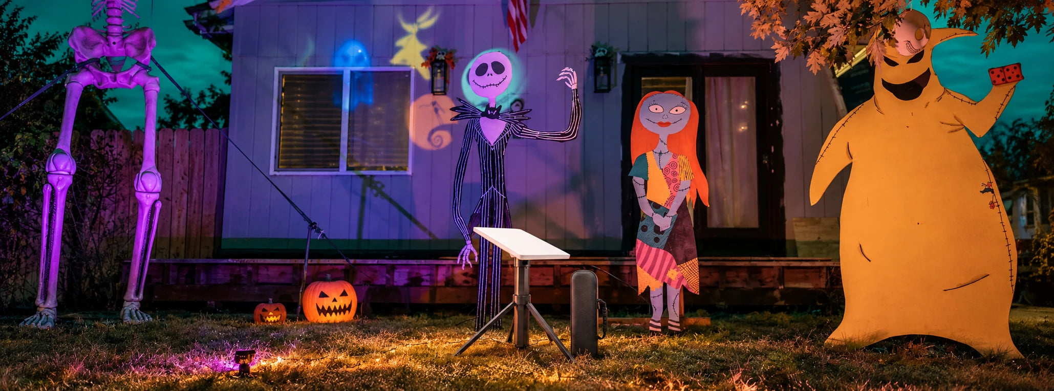 Realistic Halloween front yard with large skeleton and cartoon character decorations, with a CTmods battery tripod and carrying case in the lower center